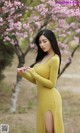 A woman in a yellow dress standing in front of a tree.