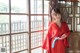 A woman in a red kimono standing in front of a window.