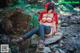 A woman in a red riding hoodie is sitting on a rock.