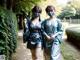 Two women in kimonos walking down a path in a park.